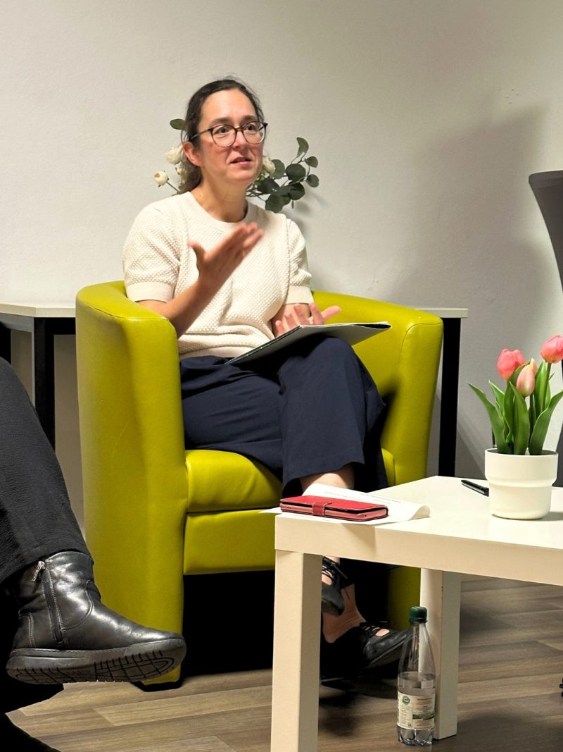 Claudia sitzt auf einem grünen Stuhl und gestikuliert beim Sprechen