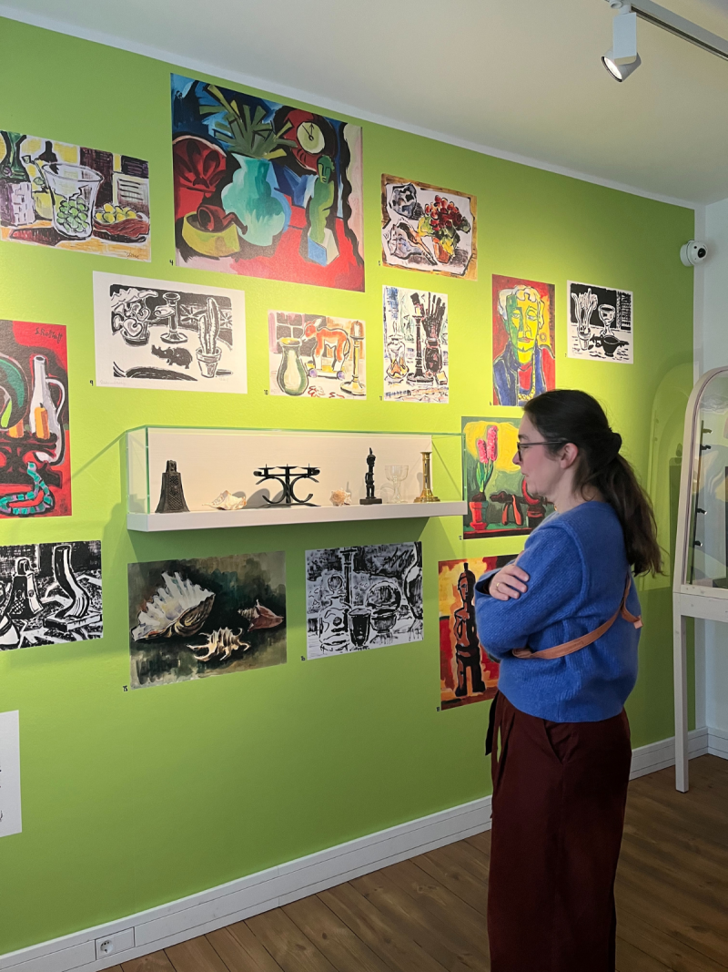 Claudia Maicher steht vor einer Wand, auf die verschiedene Werke von Karl-Schmidt-Rotluff gedruckt sind